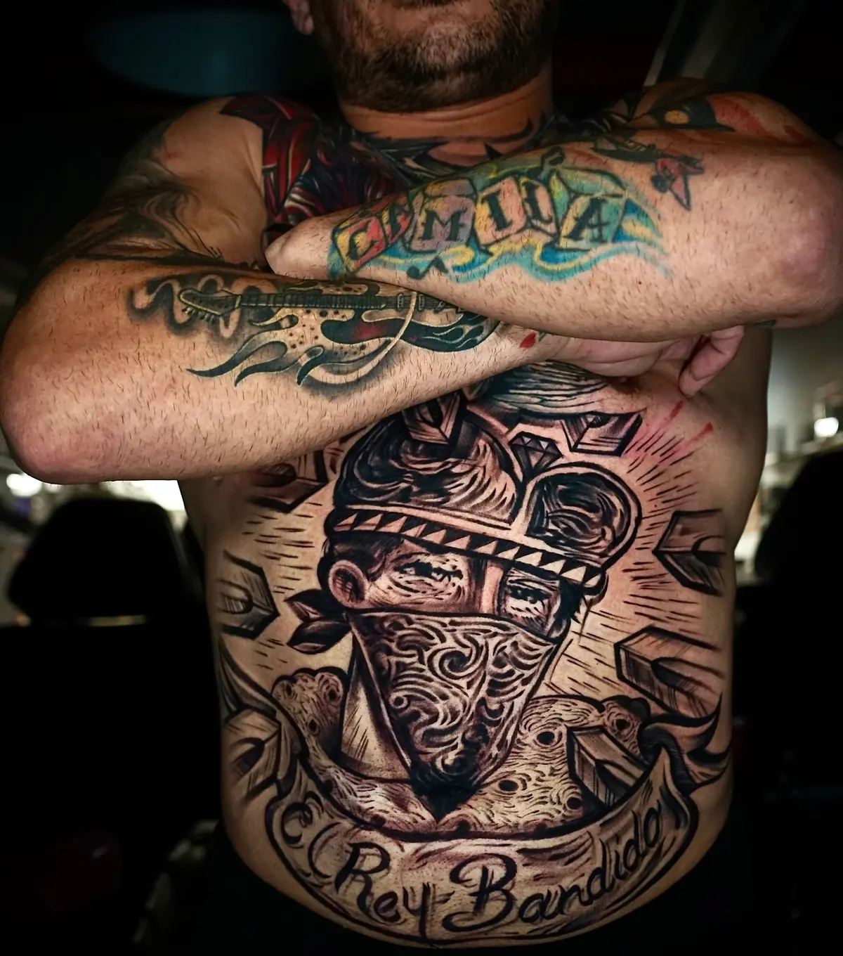 Large black and grey Chicano-style chest tattoo with a masked figure, dove, diamond, and geometric details