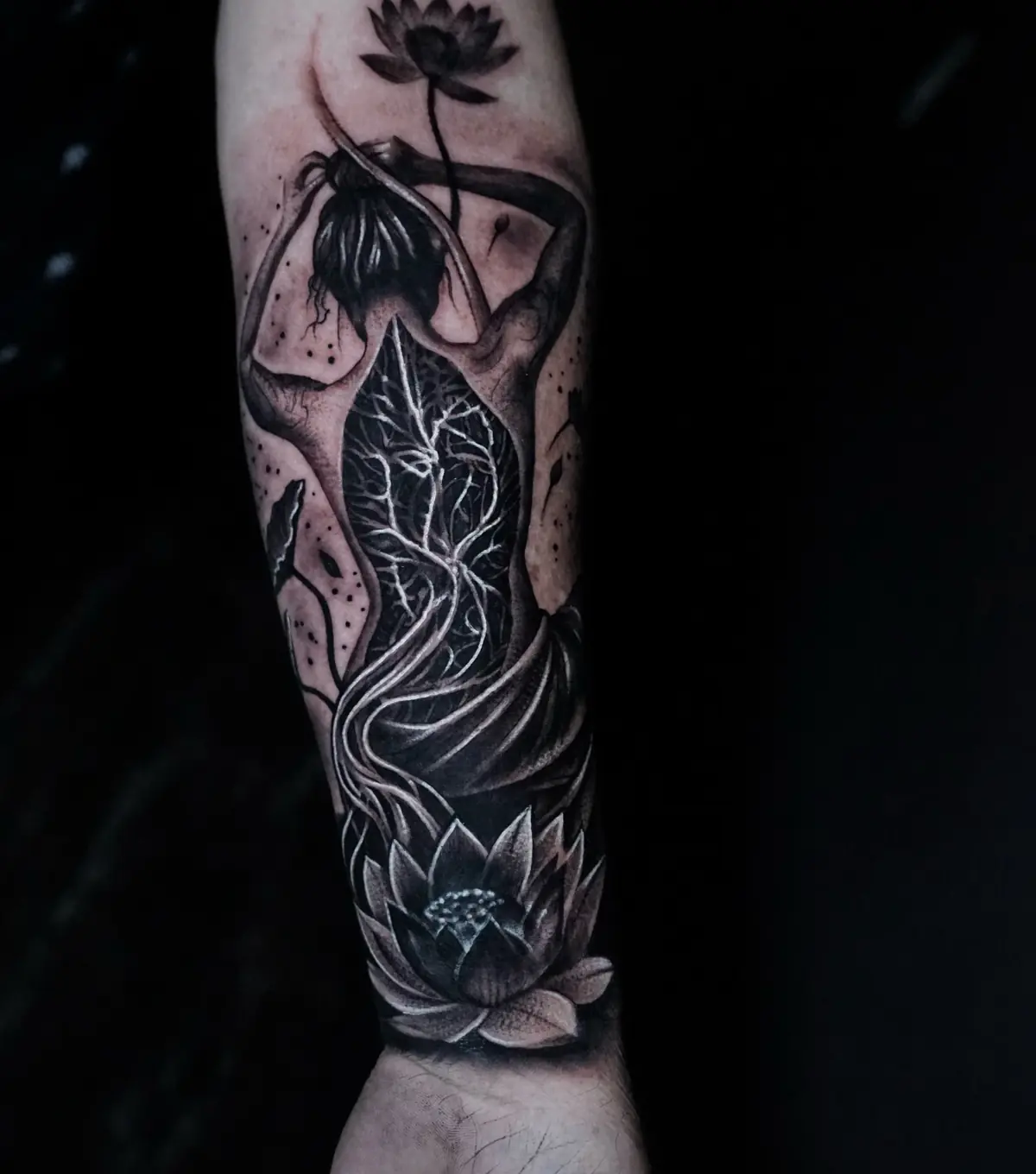 Blackwork forearm tattoo of a seated woman framed by lotus flowers and organic branches
