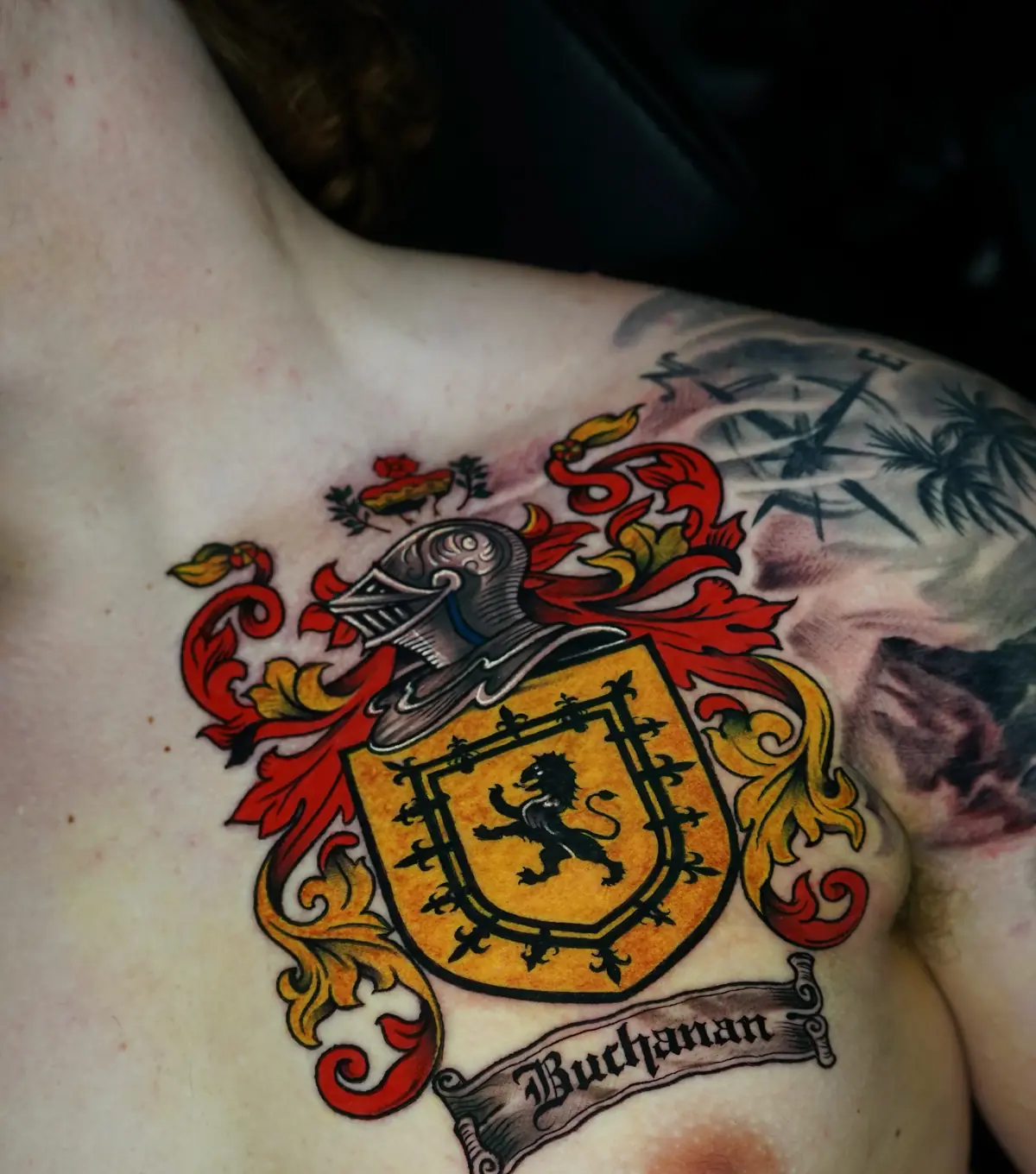 Color family crest tattoo with a helmet, lion shield, and red and yellow ornamental flourishes