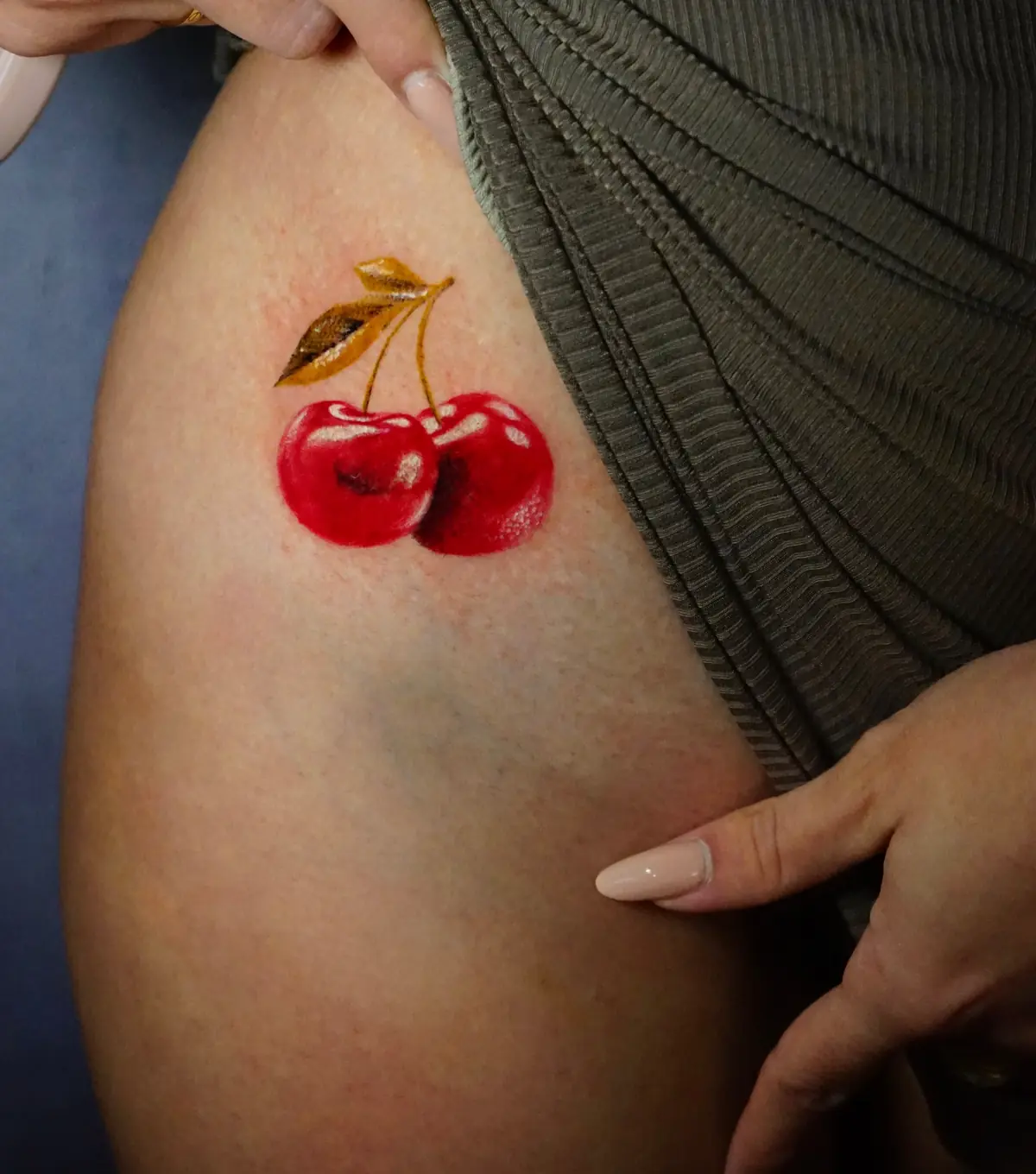 Small red cherry tattoo with golden leaves on the upper thigh