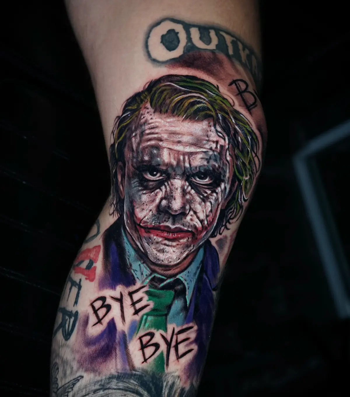 Realistic color Joker portrait tattoo with green hair, purple clothing, and handwritten details