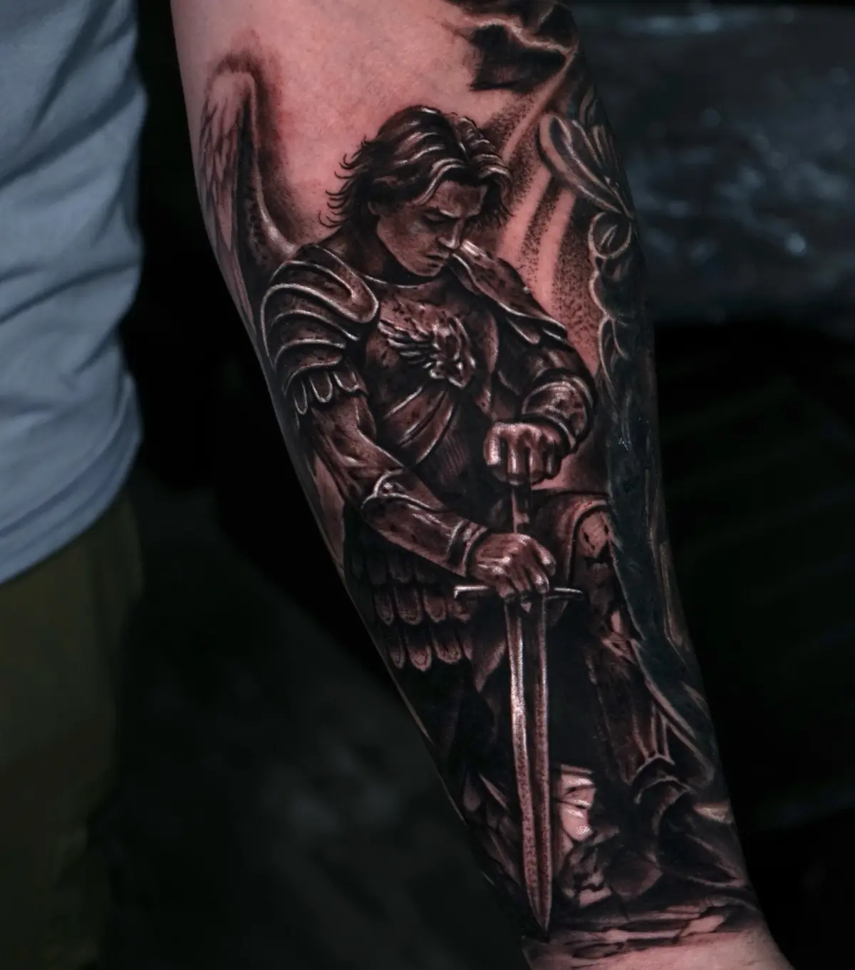 Black and grey realistic warrior angel tattoo holding a sword on the forearm